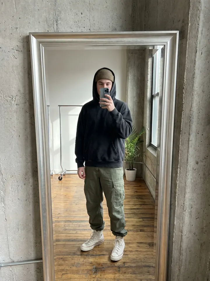 Mirror selfie of a man in a black hoodie, beanie, olive cargo pants and white high-top sneakers